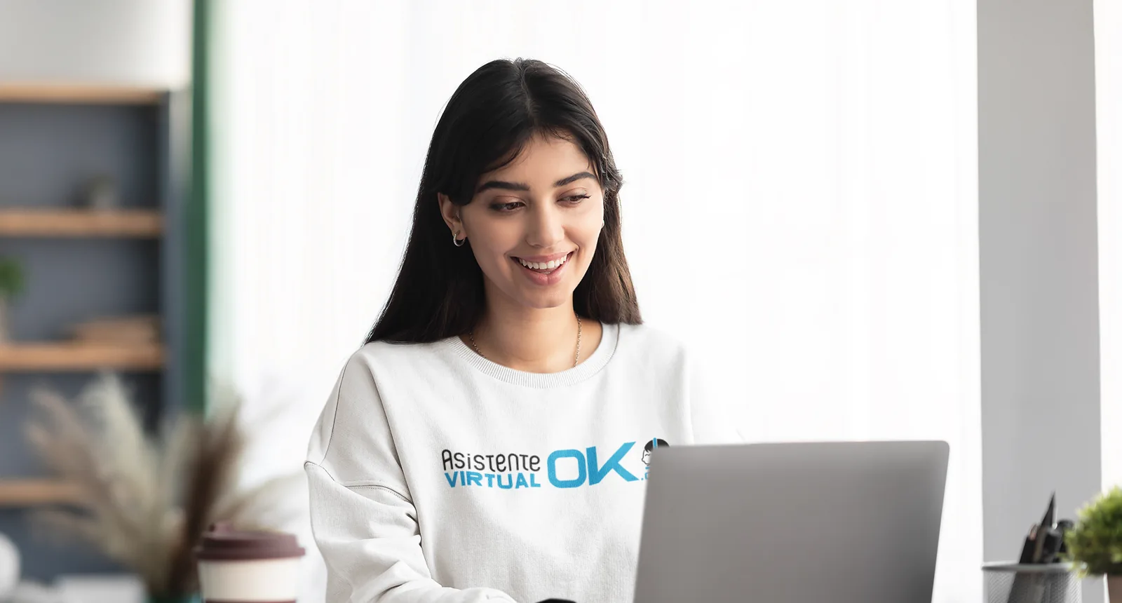 Asistente latina joven sonriendo mientras trabaja desde casa — únete al equipo AVO